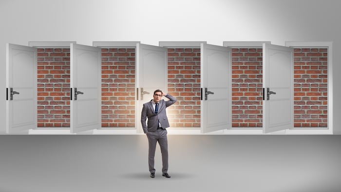 person in business suit facing open doorways that lead straight to a brick wall conveying "no exit" concept.