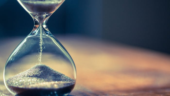 Sand running through the bulbs of an hourglass measuring the passing time in a countdown to a deadline, on a dark background with copy space.